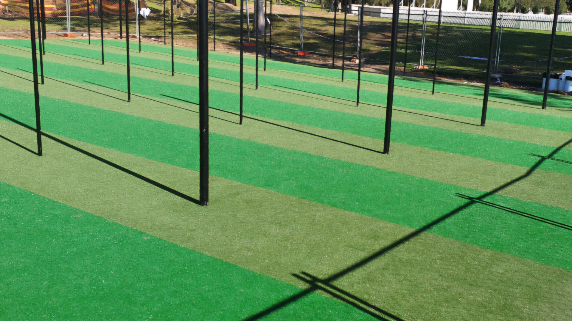 Empty green sports field with netted poles and long shadows in bright sunlight