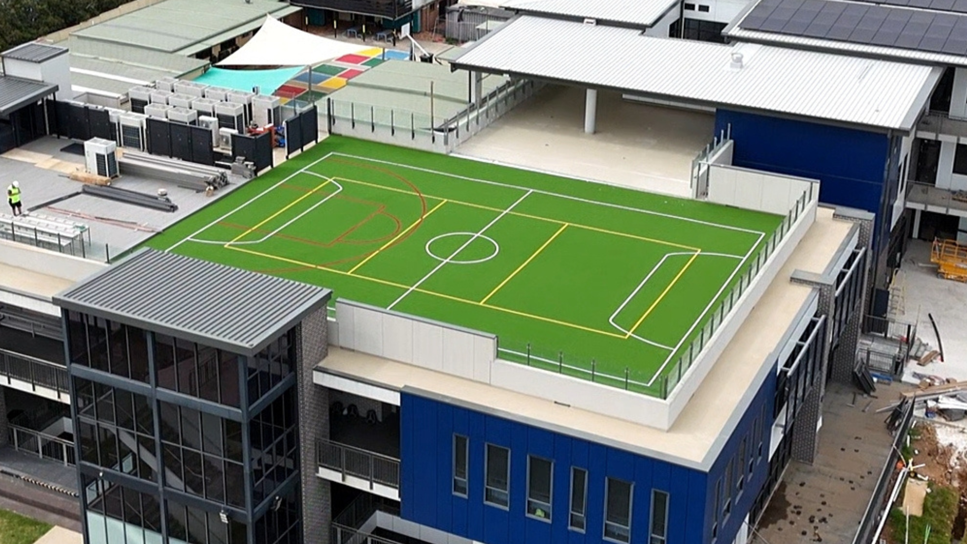 Aerial view of a rooftop sports field with green turf and orange lines atop a building.