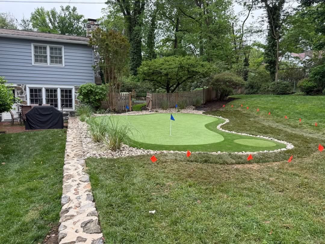 Backyard putting green with white border stones beside a house and grassy lawn