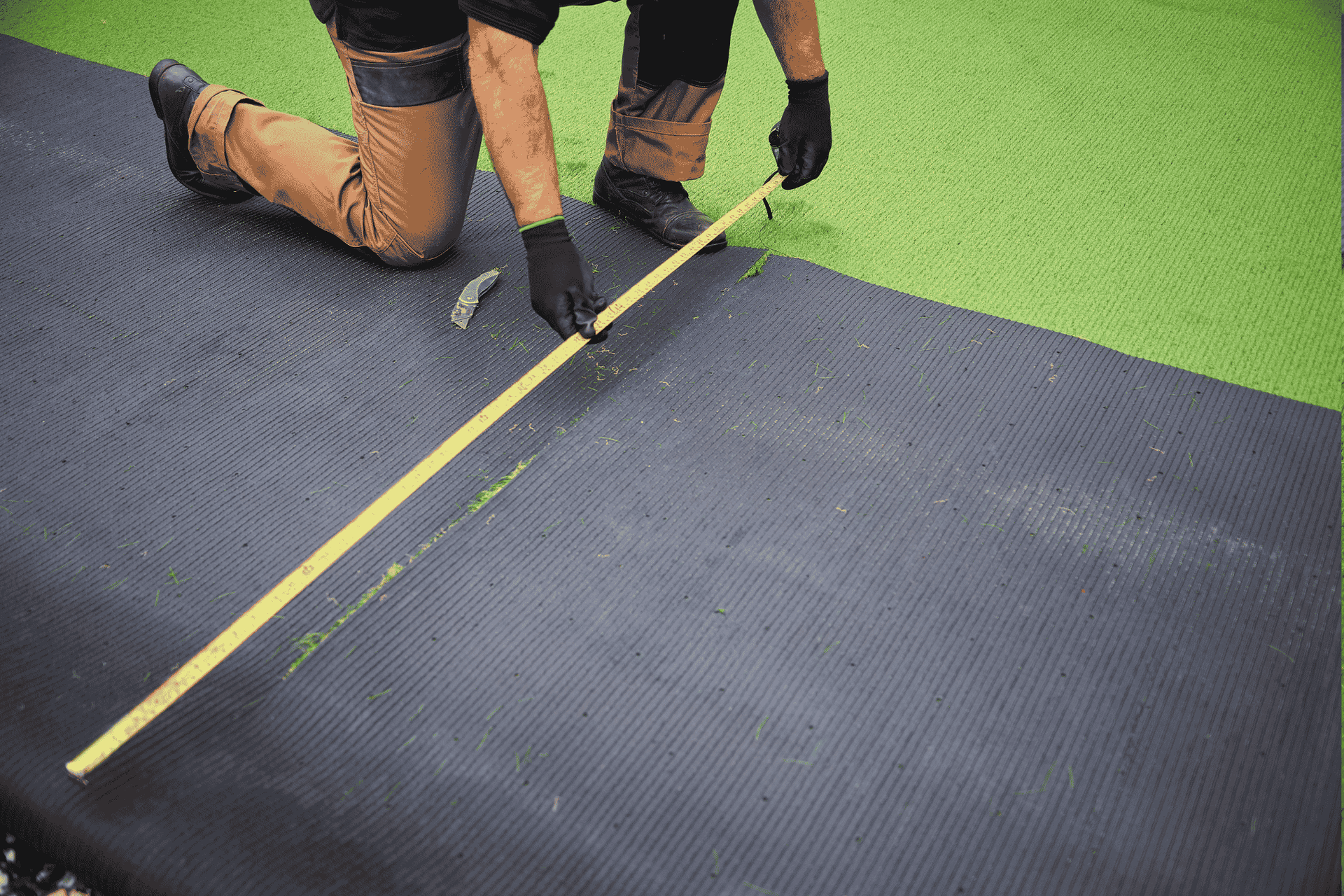 A man measuring the length of a green synthetic grass mat with a ruler, ready for installation in Sydney.