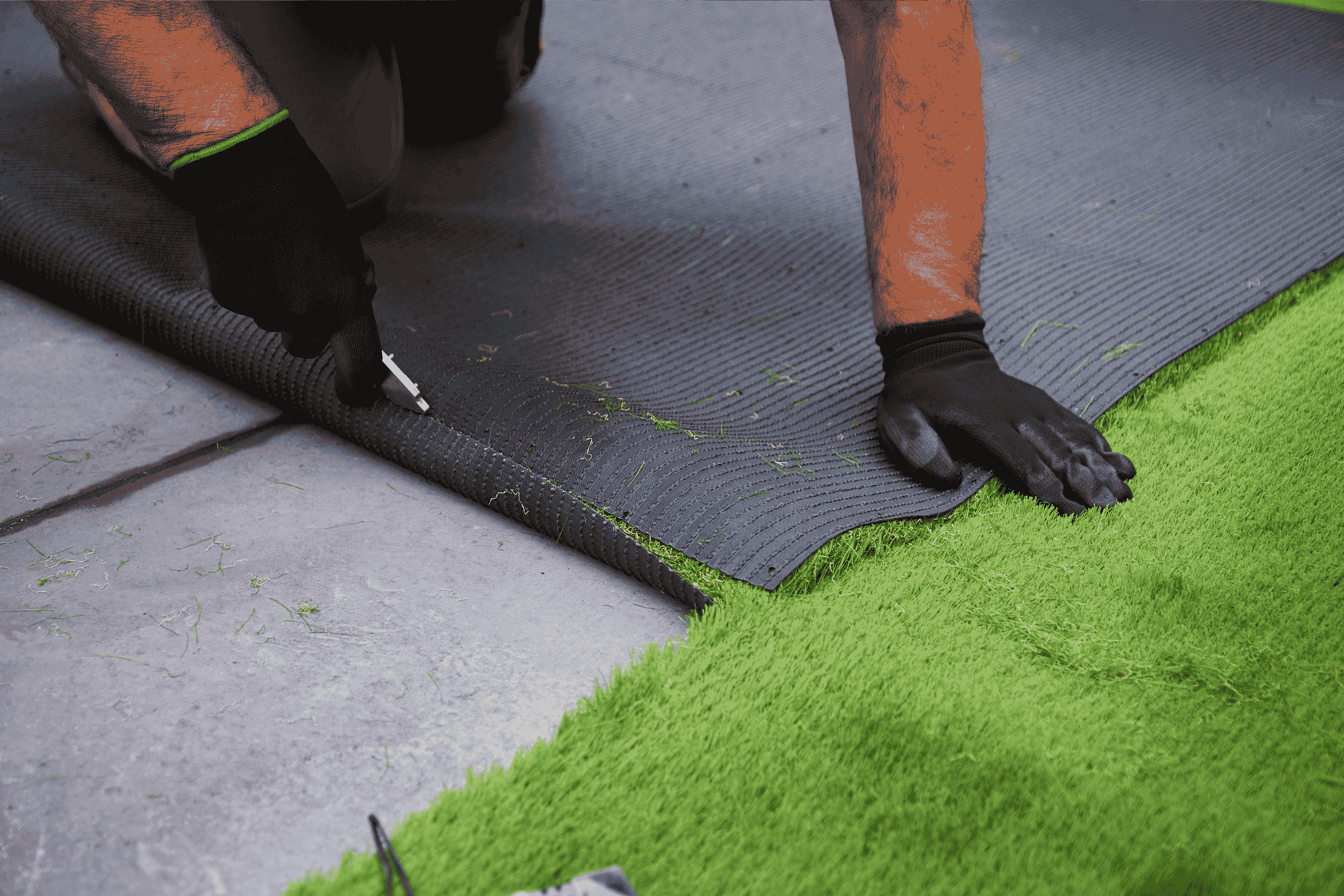Close-up of a person carefully trimming synthetic grass on a green rug, illustrating installation st