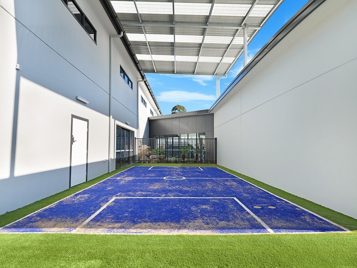 Blue artificial turf court between two white buildings under a covered walkway