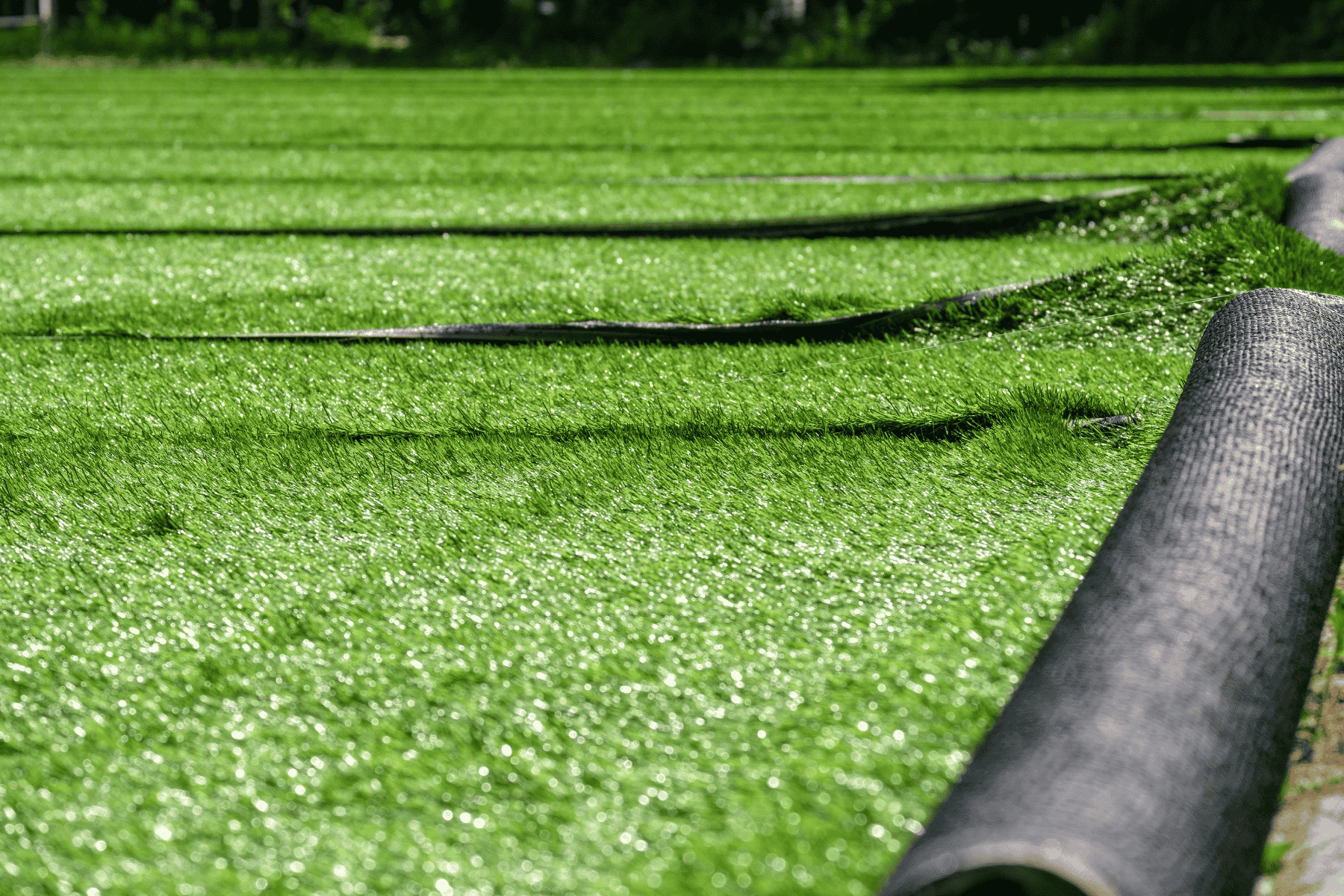 Black pipes are arranged in a long line within a grassy field, indicating preparation for synthetic grass installation