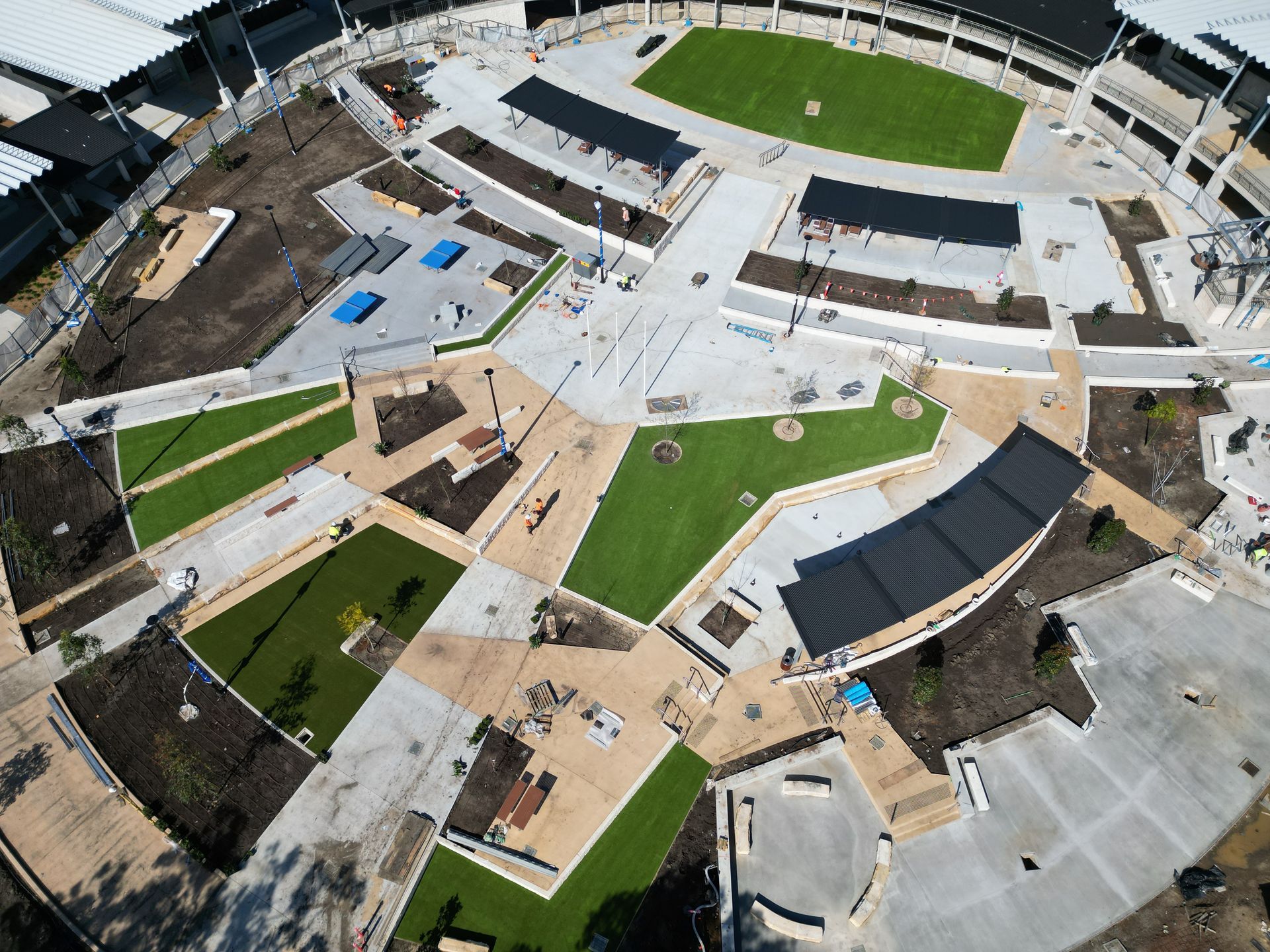 Aerial view of a modern outdoor plaza with green lawns, paths, benches, and surrounding buildings