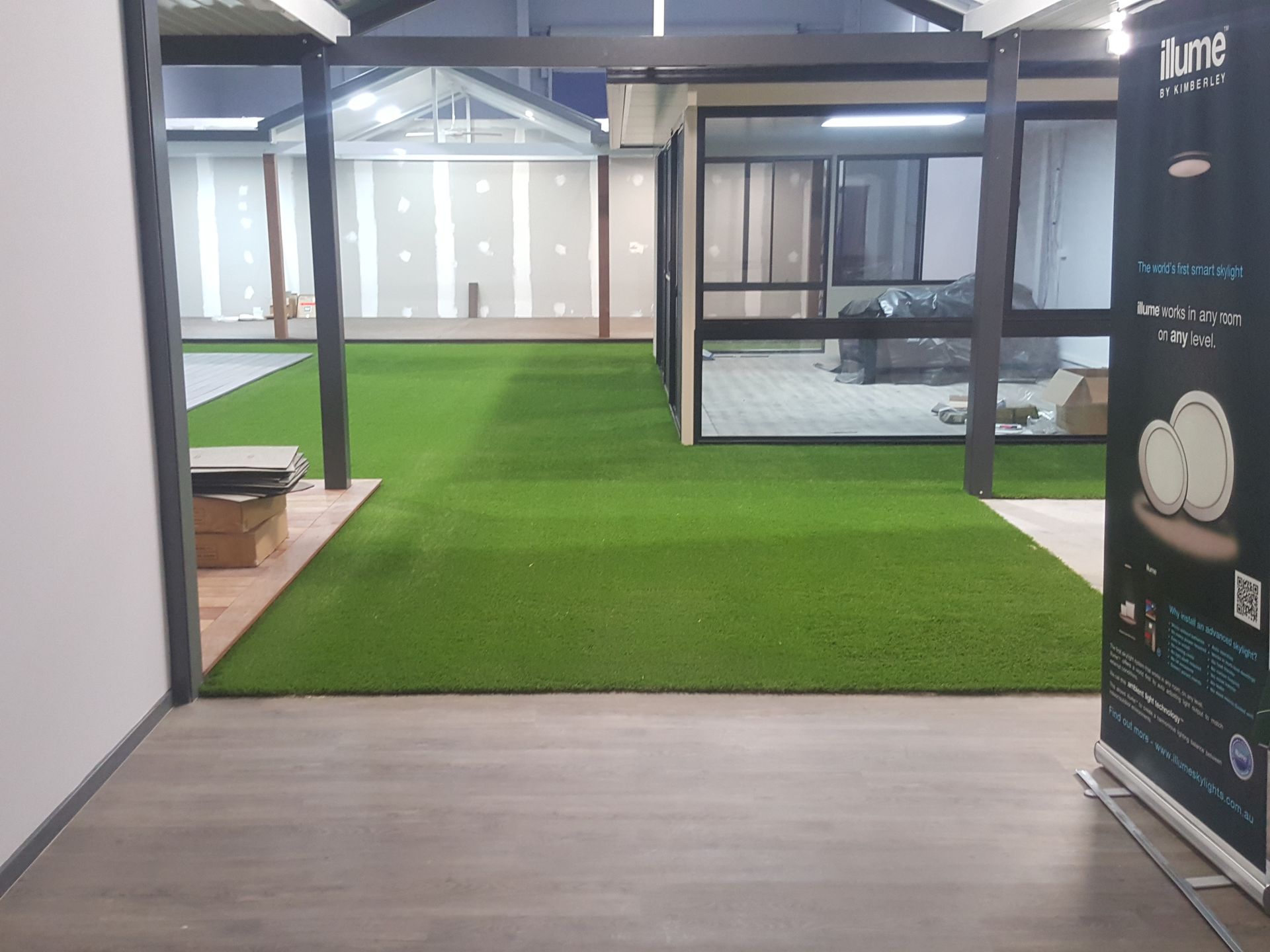 Indoor lobby with green artificial grass, glass-walled rooms, and wood flooring.