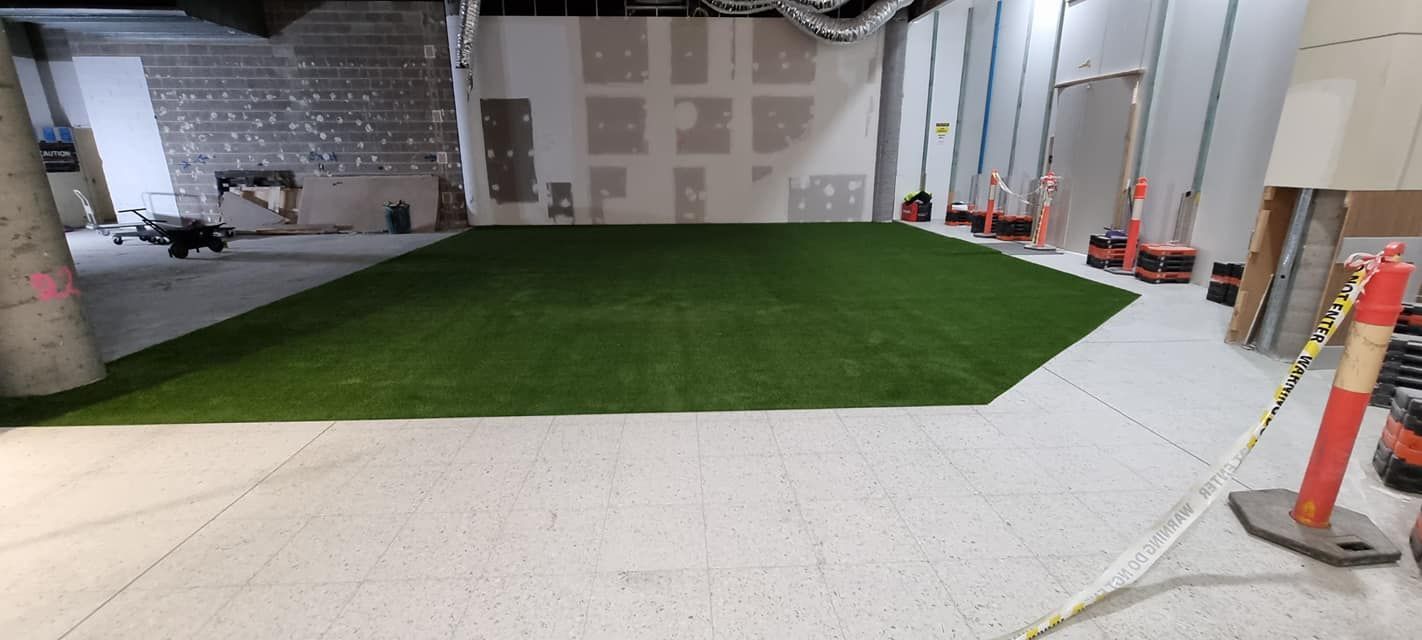 Indoor construction area with green turf and white flooring, marked by orange cones and unfinished walls