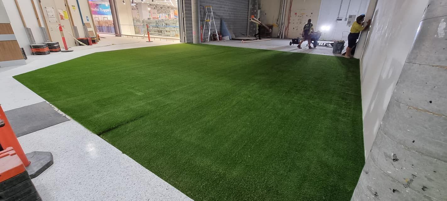 Indoor space with a large green turf area bordered by white flooring and concrete walls