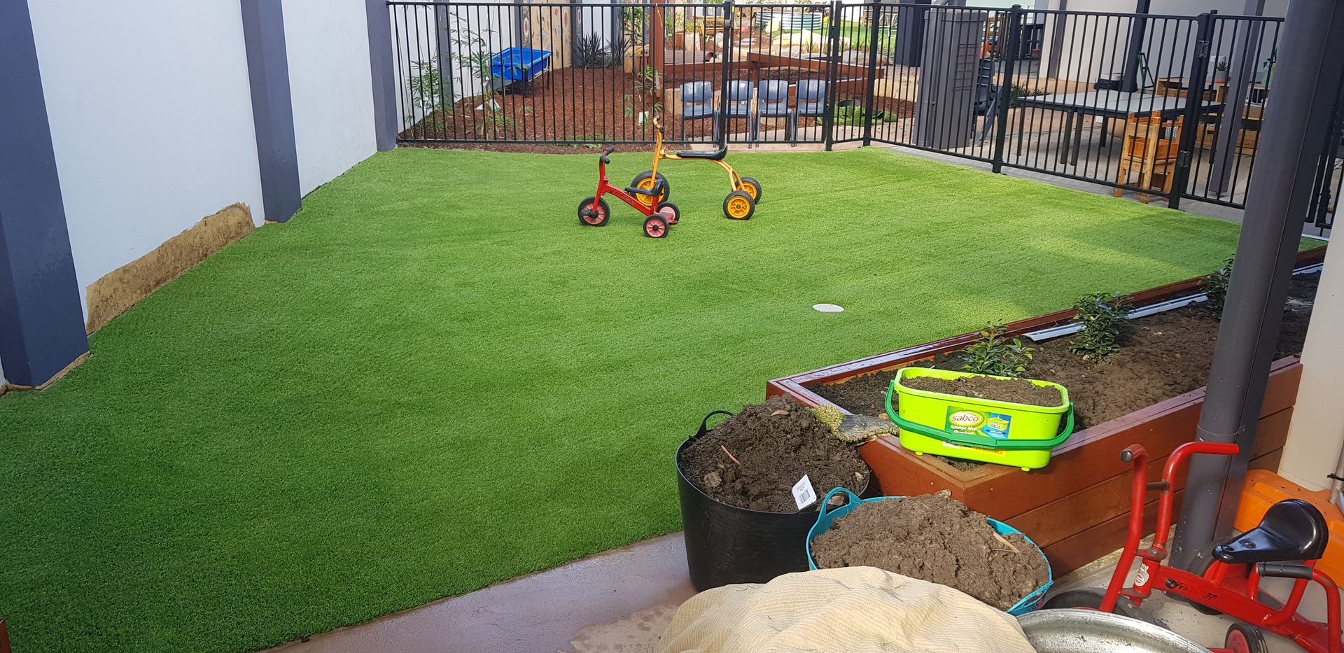 Outdoor patio with artificial grass, children’s toys, and a fenced seating area