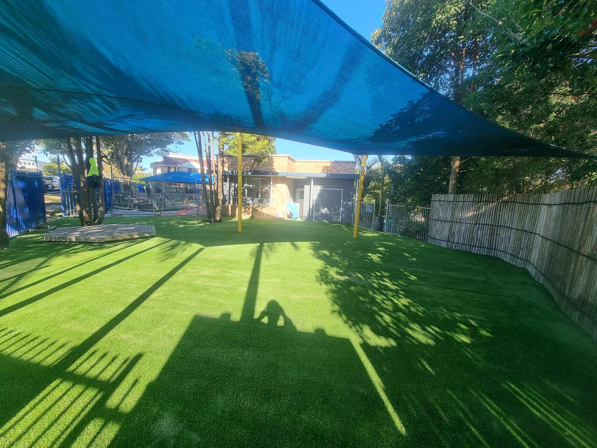 Shaded backyard lawn with green grass, blue canopy overhead, trees, and a stone wall along the side