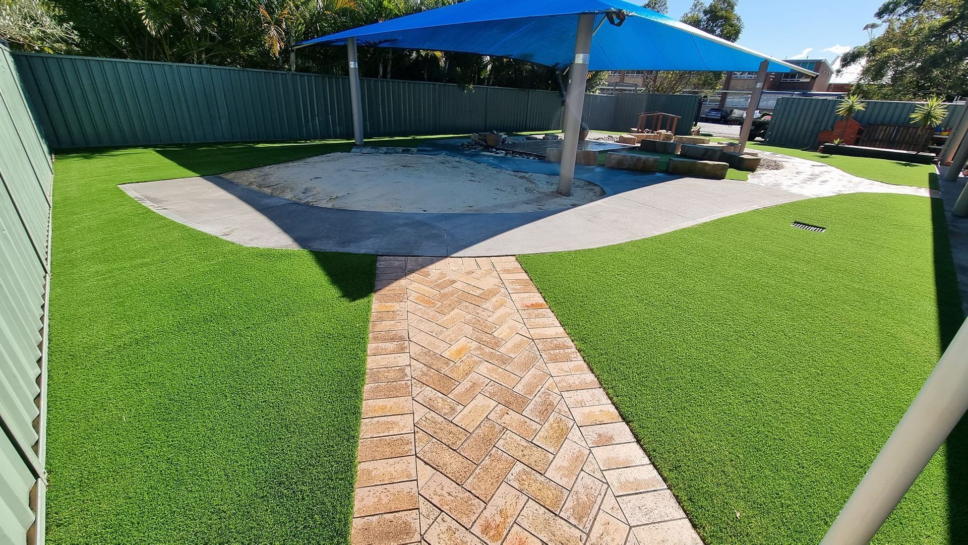 Backyard patio with green lawn, brick path, and blue umbrella over a paved seating area