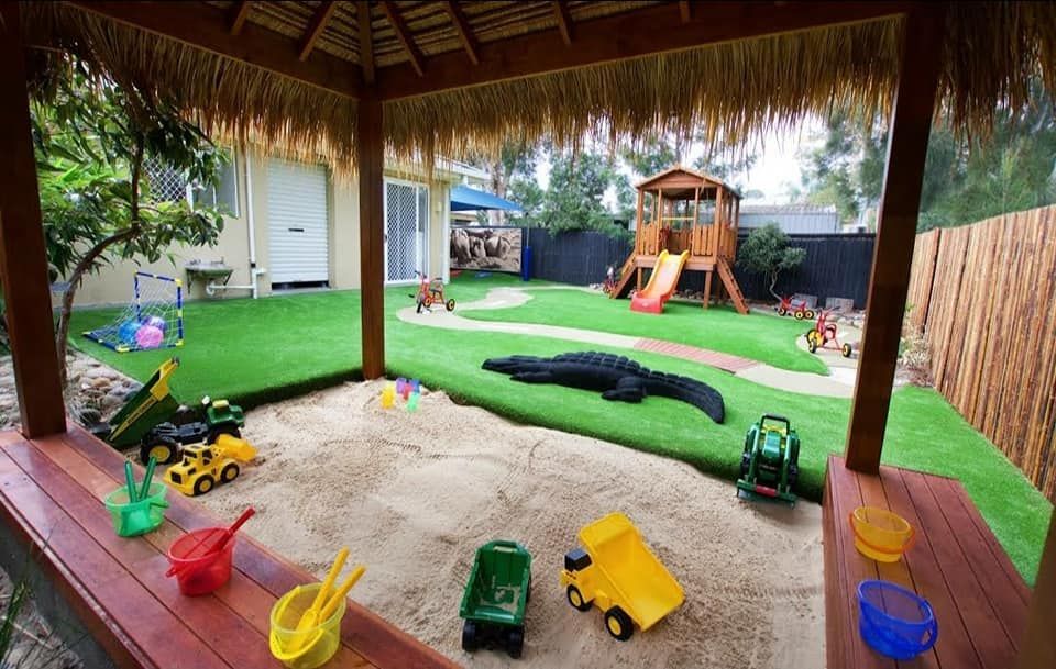 Covered backyard play area with toy vehicles, sandbox, and a playground in the grass outside