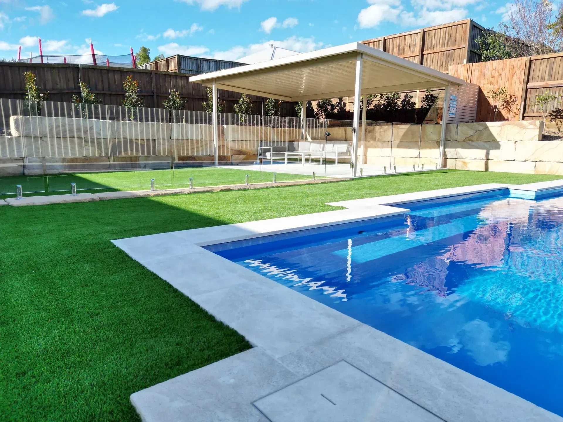 Backyard pool with blue water, green turf, and a shaded seating area under a canopy