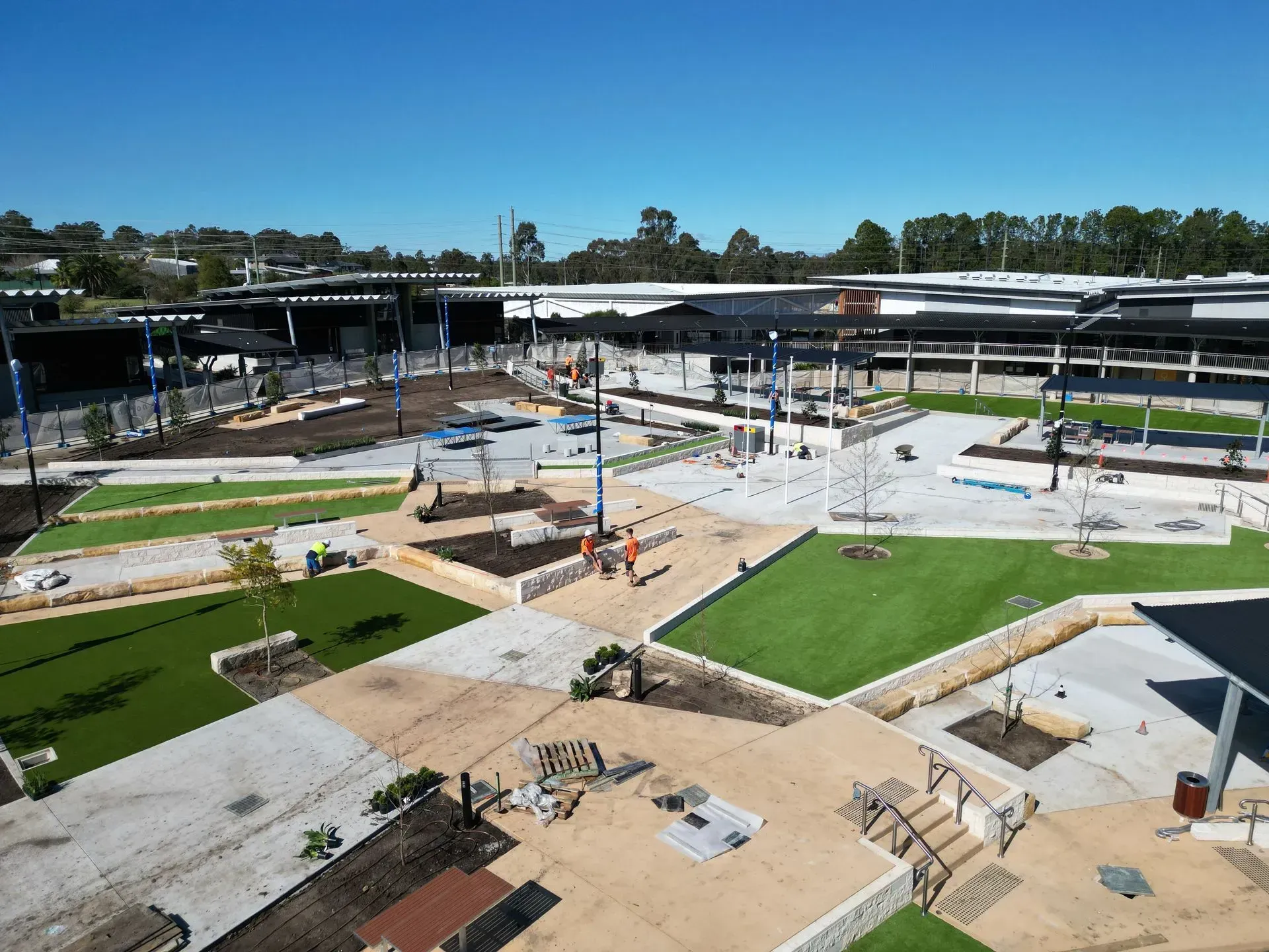 Outdoor construction site with concrete walkways, grass plots, and steel frames under a blue sky