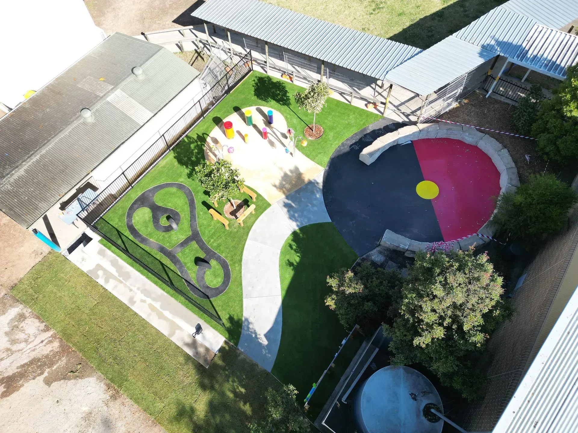 Aerial view of a colorful playground with green lawn, play structures, and a round black-and-pink play area