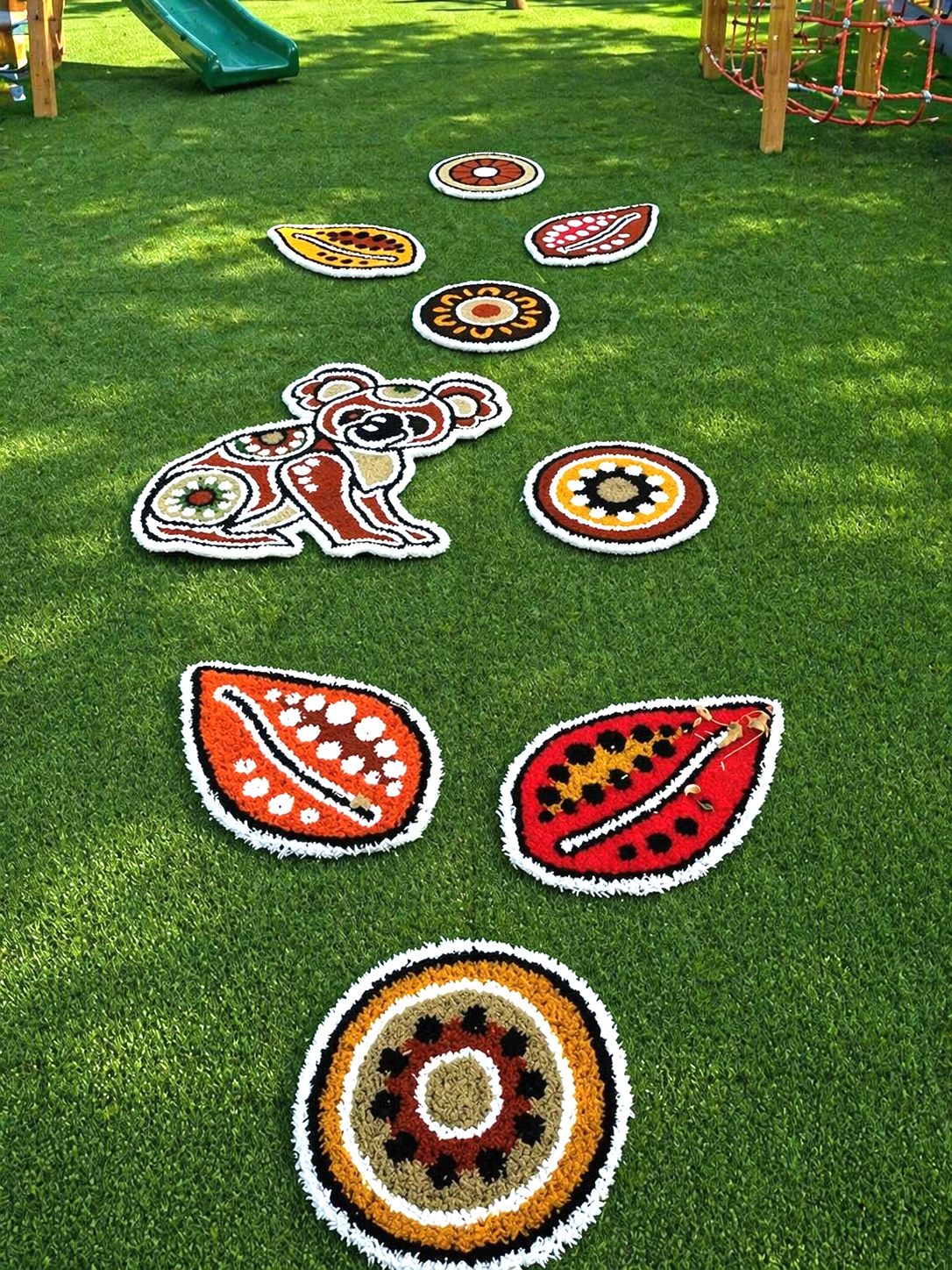 Colorful rangoli-style animal and leaf designs arranged on grass in a park or playground