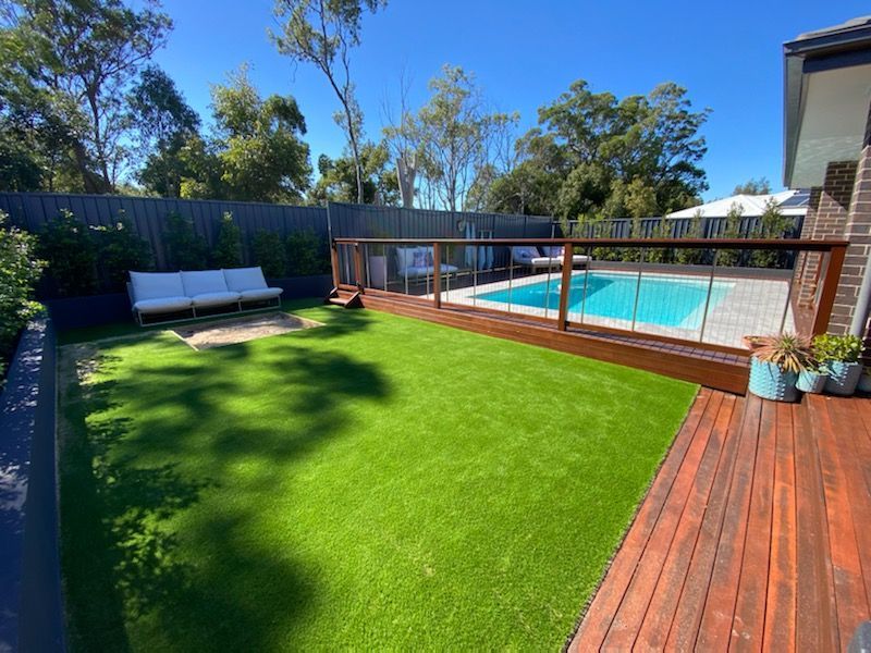 Backyard with bright green lawn, wooden deck, pool, and lounge chairs under a clear blue sky