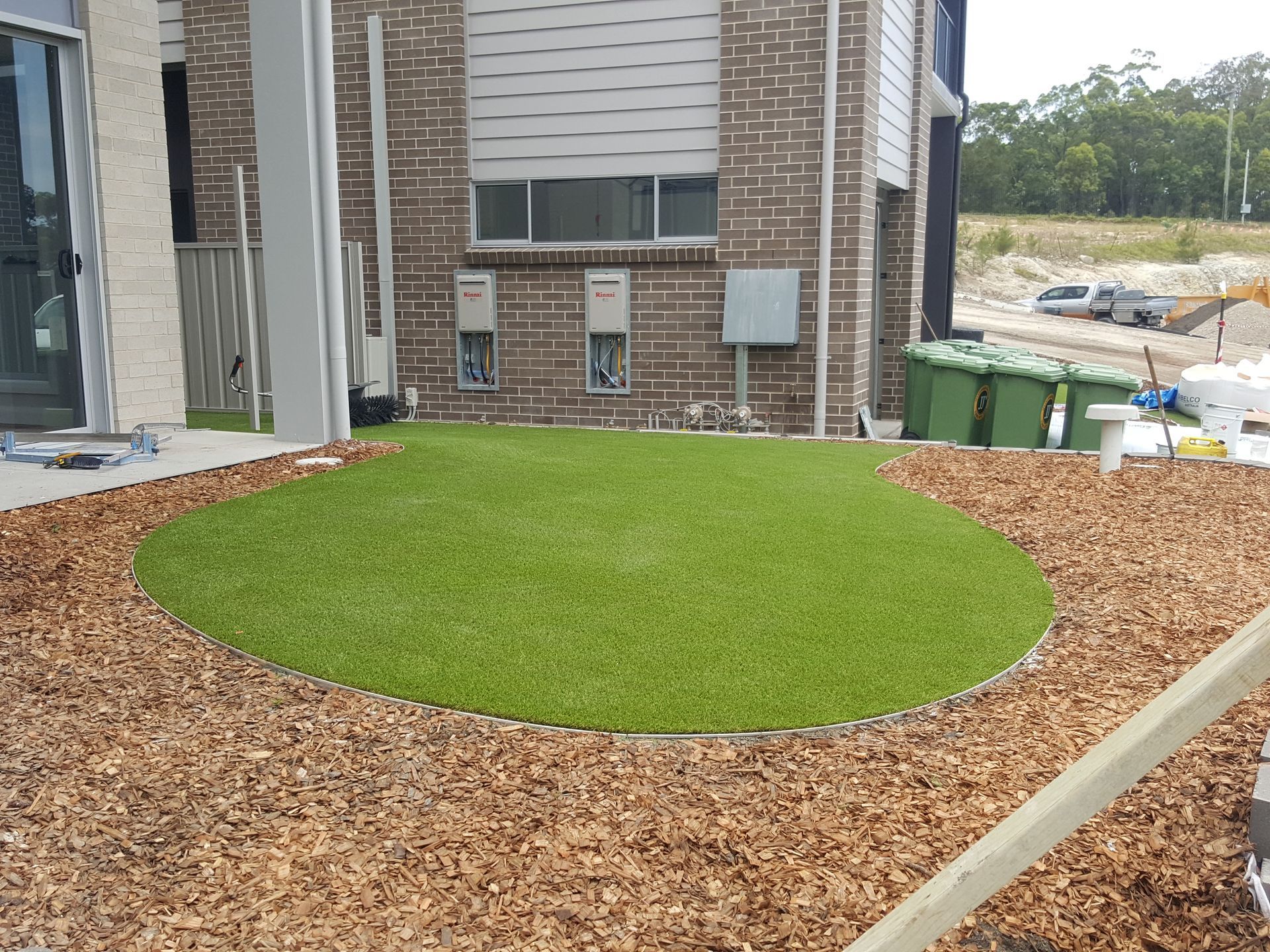 Newly landscaped yard with a circular patch of green sod surrounded by mulch beside a brick building