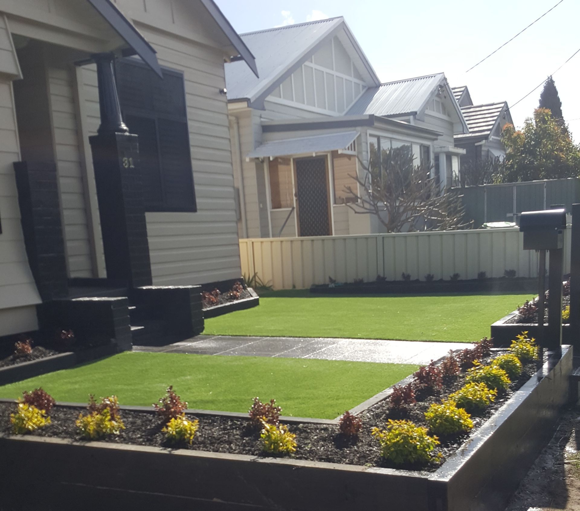 Front yard with artificial grass, raised flower beds, and suburban houses in the background