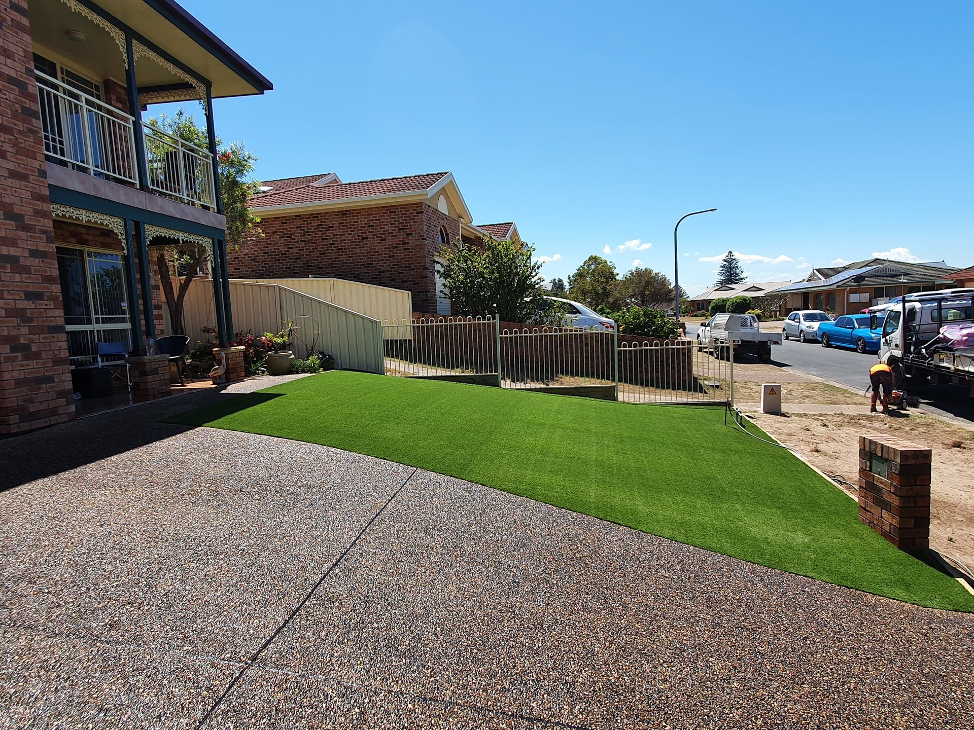 Front yard with gravel and bright green lawn beside a house, overlooking a sunny waterfront street