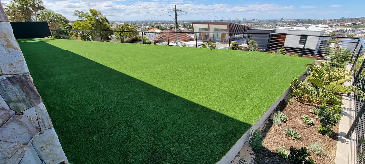 Rooftop garden with bright green artificial grass, stone wall, and city buildings in the background
