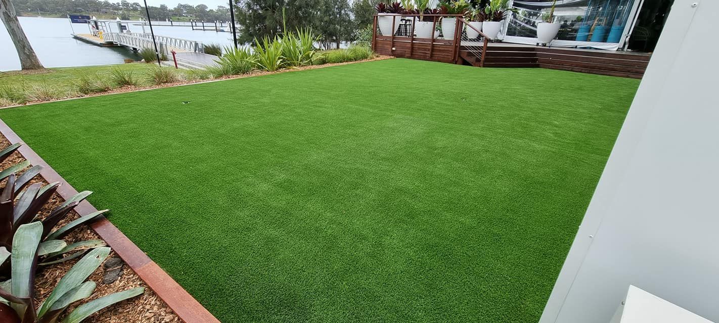 Green lawn beside a waterfront deck with plants and a white wall