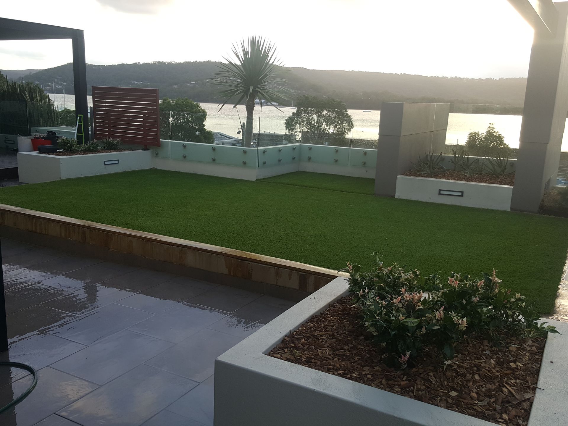Patio with artificial grass, white planters, and a wet tiled walkway beside an outdoor pool area