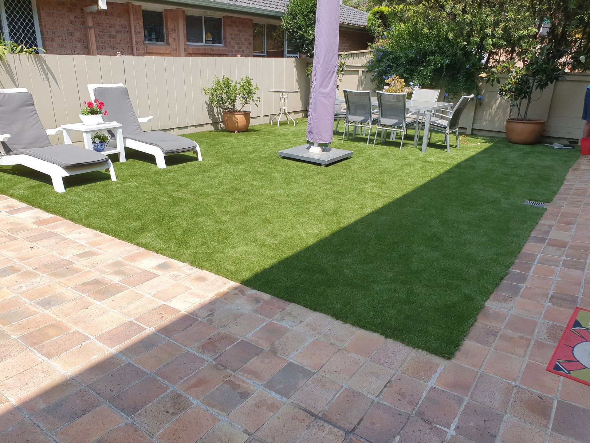 Backyard patio with green lawn, white lounge chairs, and a shaded seating area by the house.