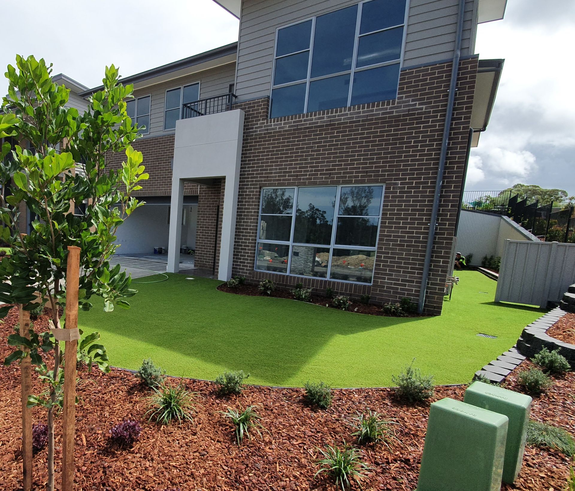 Modern two-story brick house with large windows, green lawn, and landscaped front yard