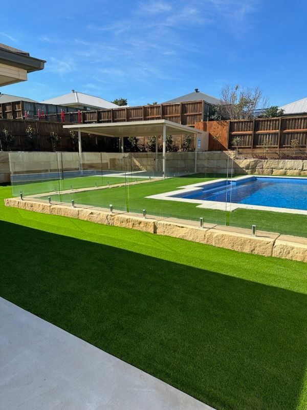 Backyard with artificial turf, patio, and covered swimming pool under a blue sky