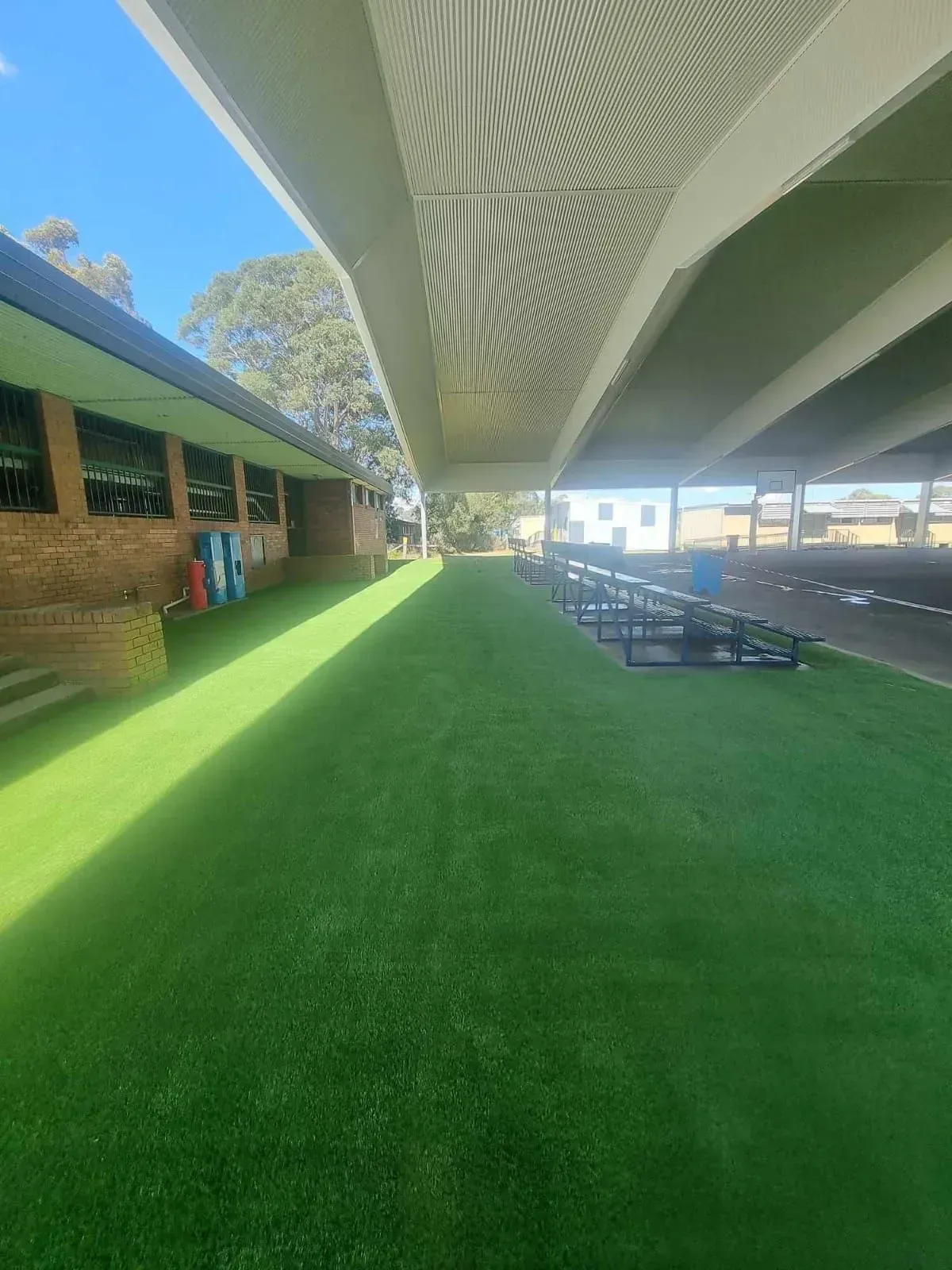 Covered outdoor walkway beside green lawn and benches at a school or stadium.