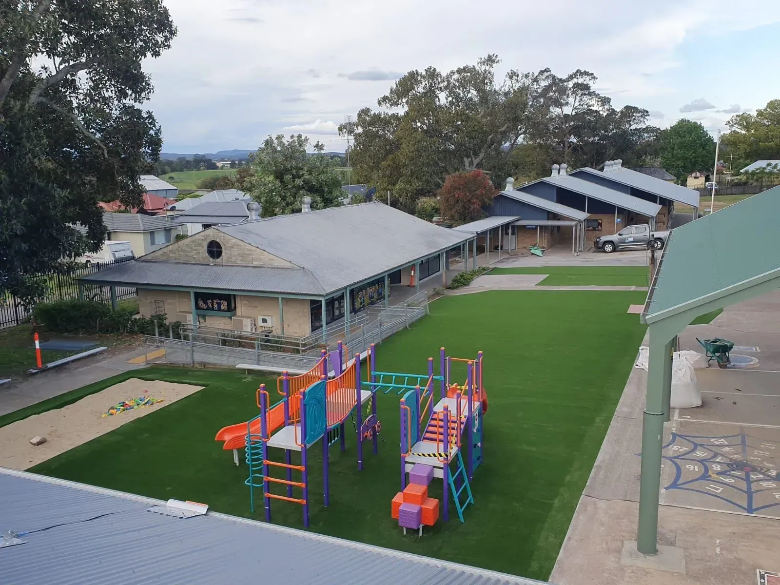 School playground with colorful climbing equipment beside classroom buildings on a cloudy day