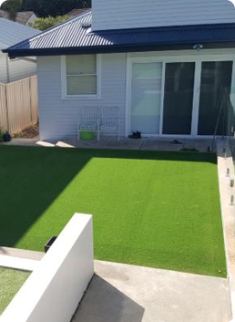 Backyard patio with artificial grass, concrete path, and a house with sliding glass doors