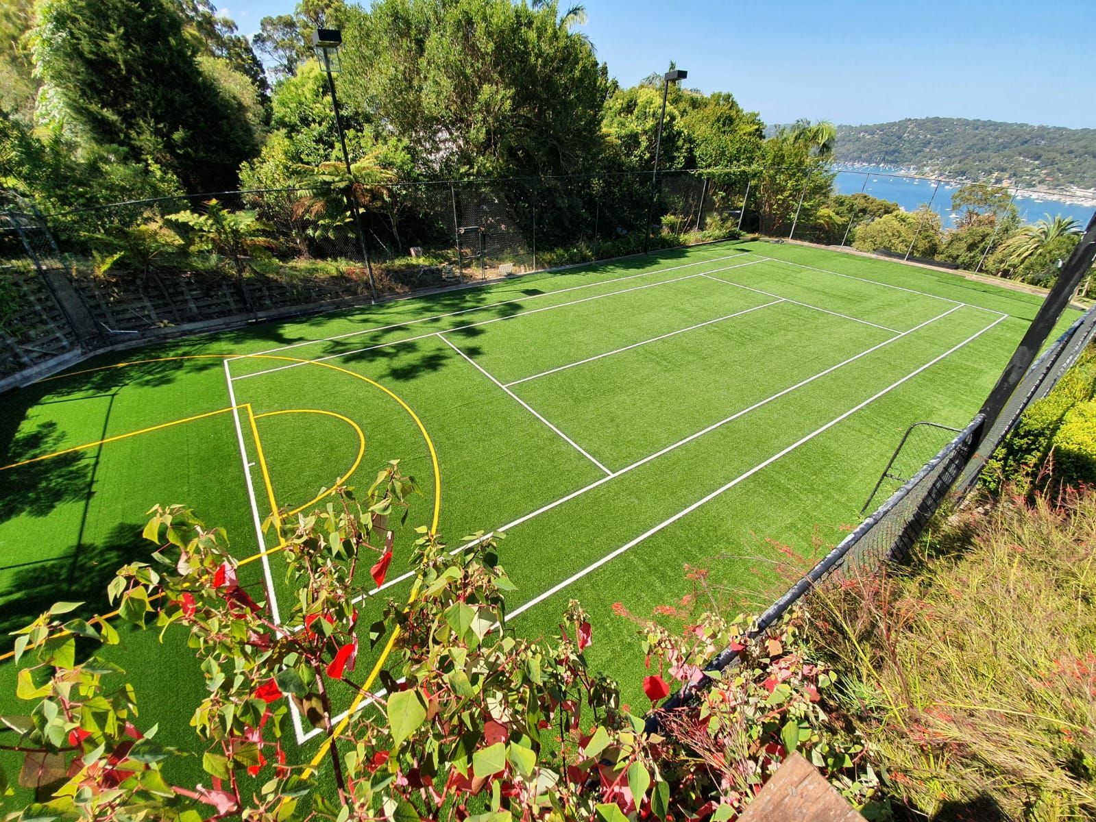 Empty green sports field with white lines on a hillside, surrounded by trees and overlooking water