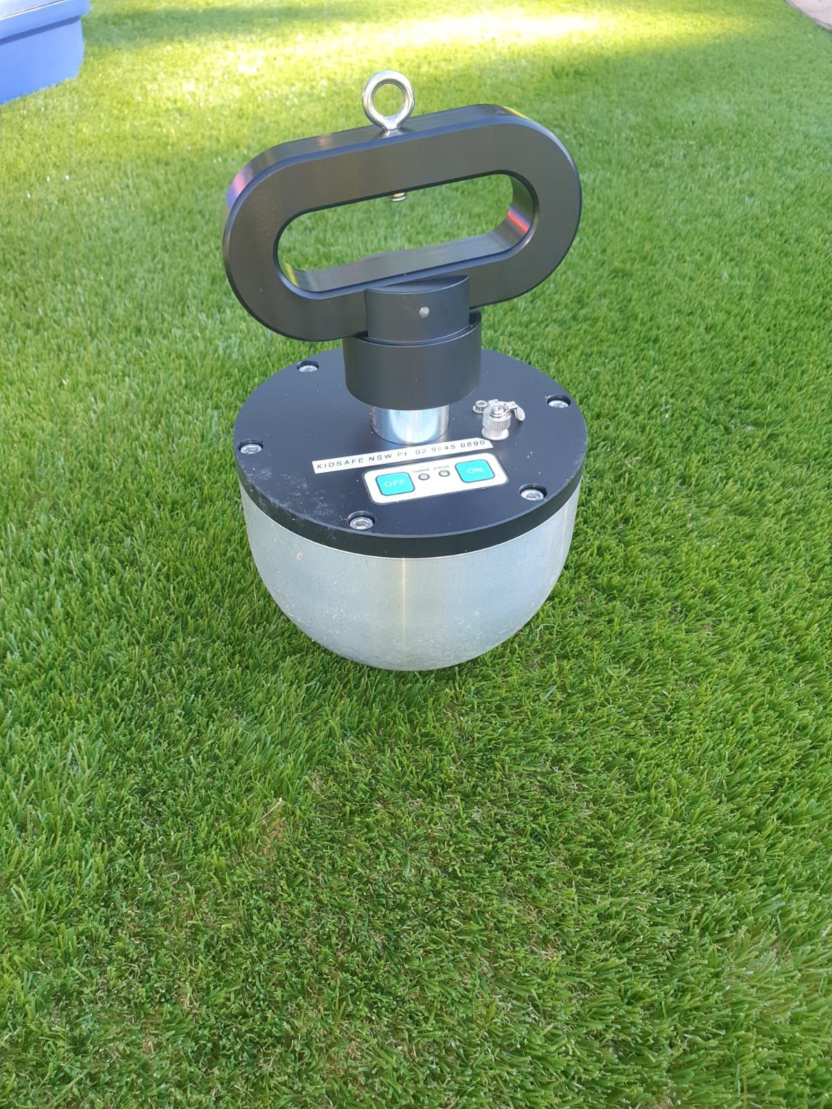 Gray surveying instrument on a grassy lawn, with a black handle and circular base.