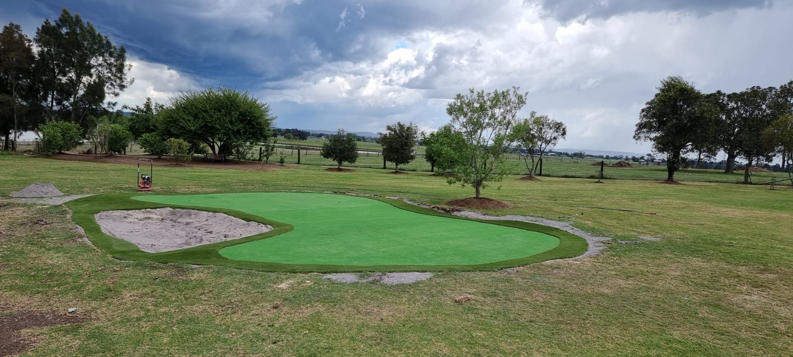 Mini golf green with sand traps on a grassy field under a cloudy sky