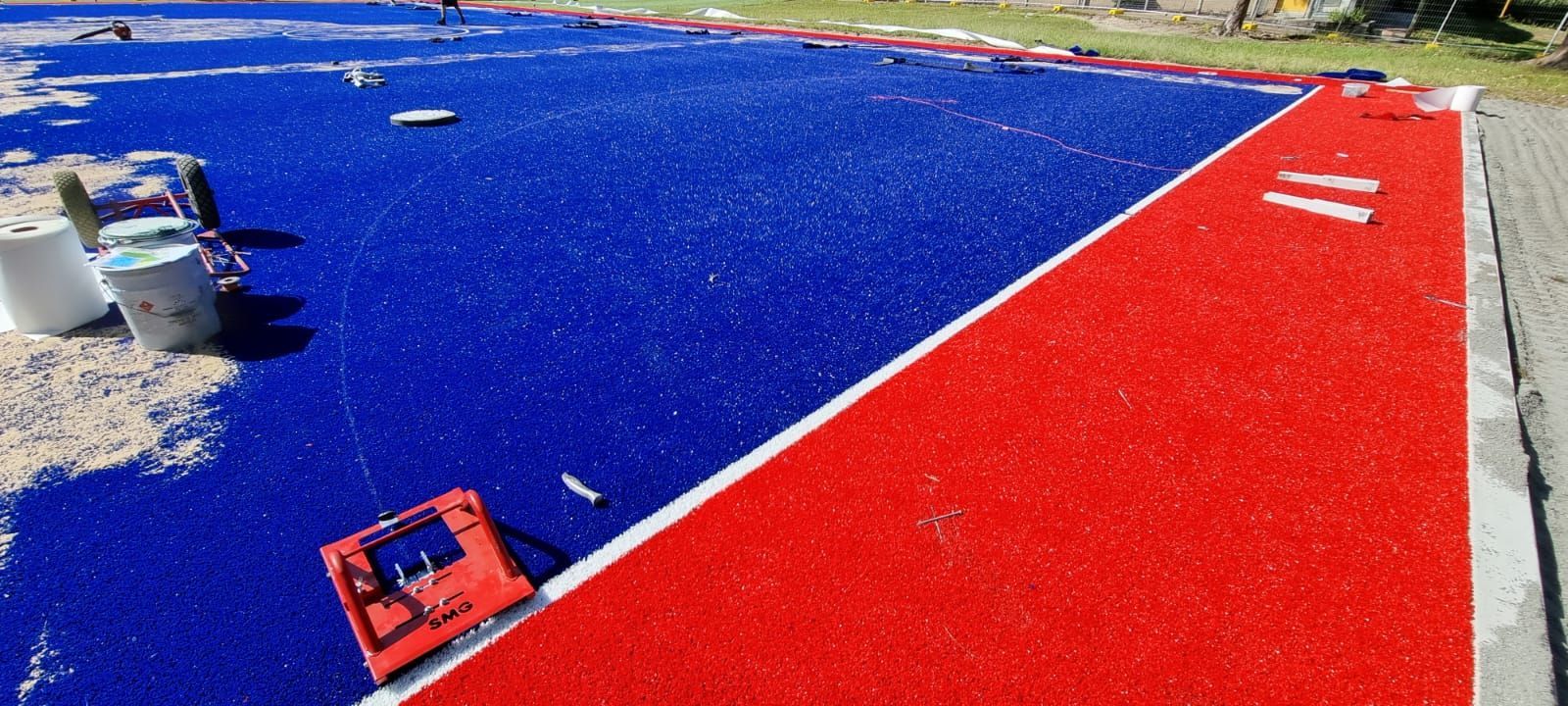 Blue and red sports court with white boundary lines and paint supplies at the edge