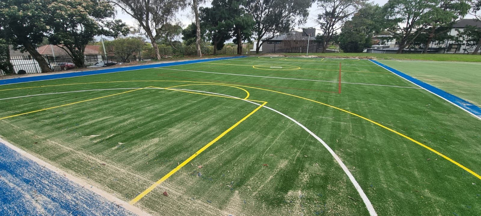 Marked sports field with white and yellow lines on green turf under trees