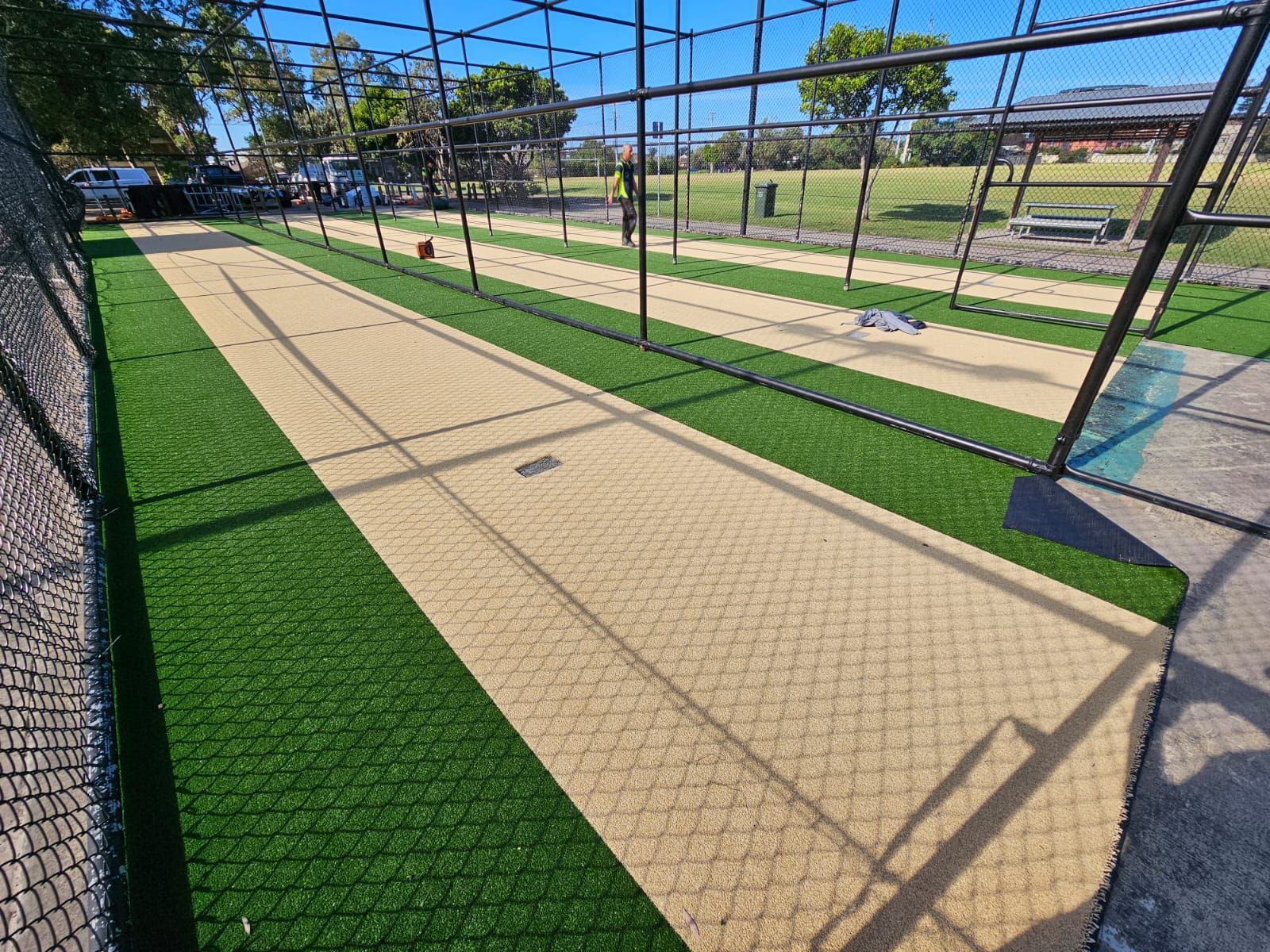Outdoor cricket practice net with tan pitch and green turf under a blue sky