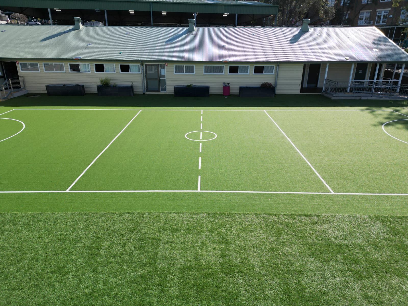 Empty green sports field with white boundary lines and a building in the background