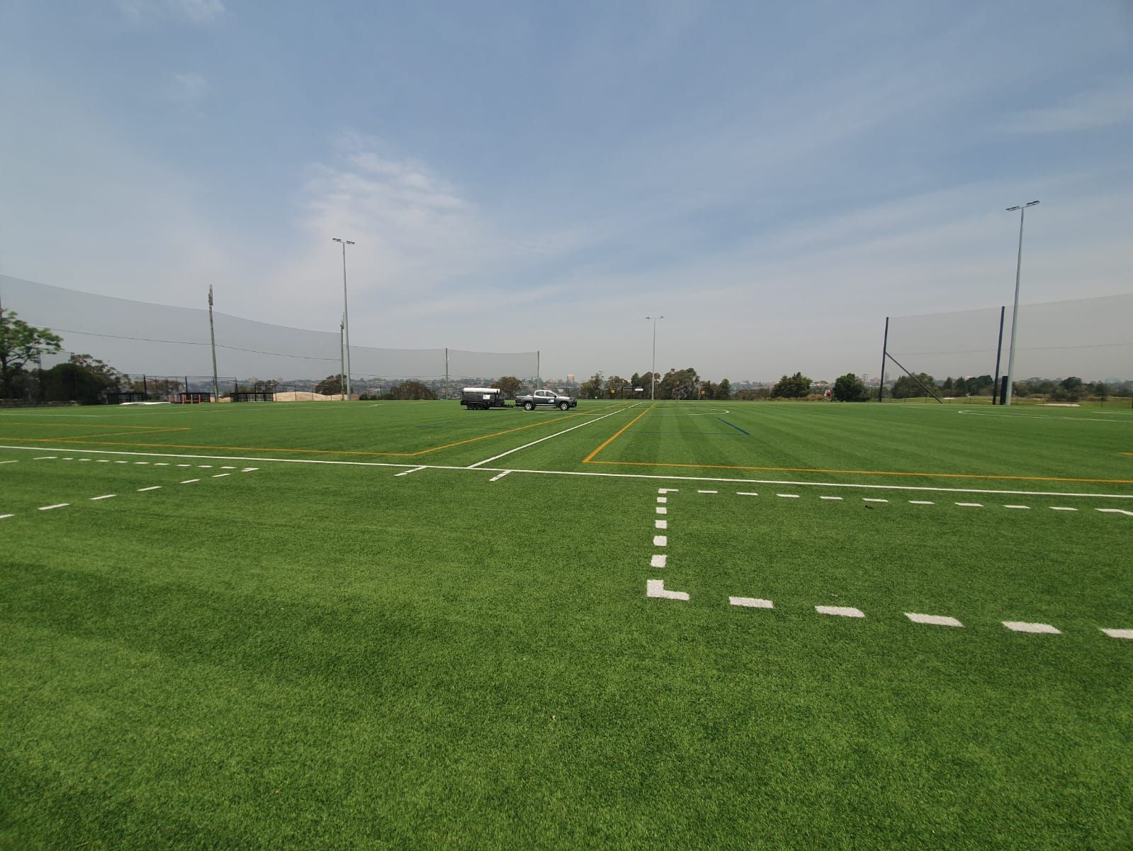 Empty green sports field with white yard lines under a hazy sky