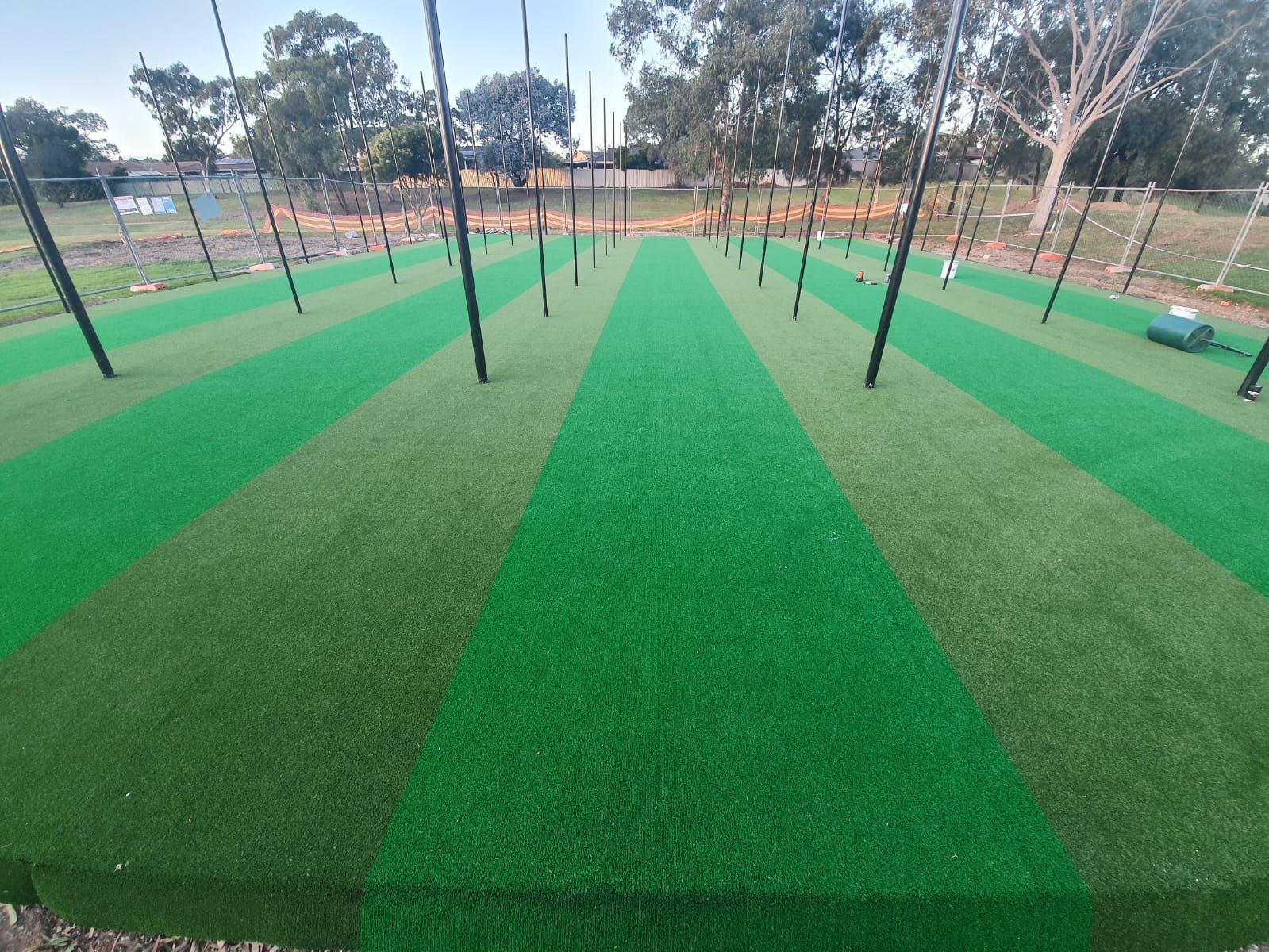 Green striped sports field with black poles and trees in the background