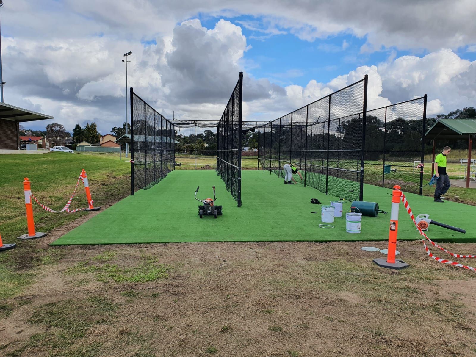 Temporary outdoor sports enclosure with black net fencing, green turf, cones, and equipment under a cloudy sky
