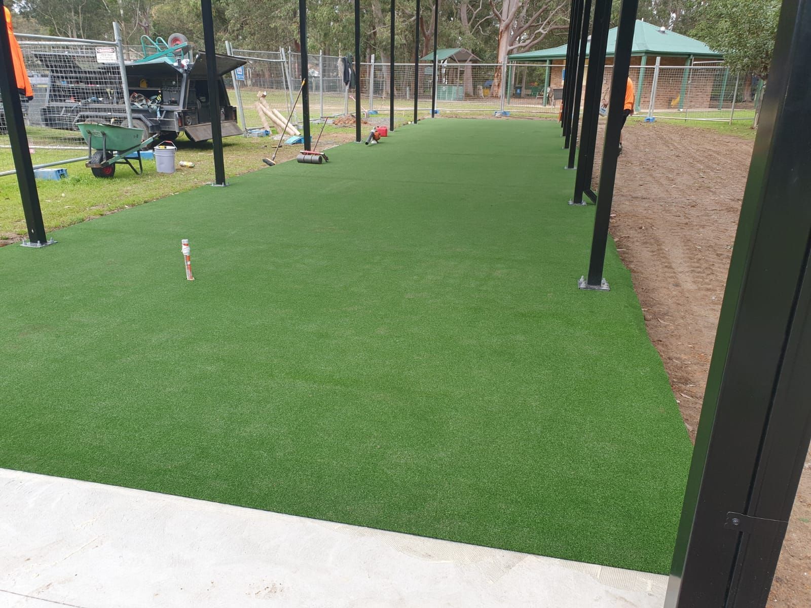 Covered outdoor patio with bright green artificial turf and a concrete edge beside a fenced yard
