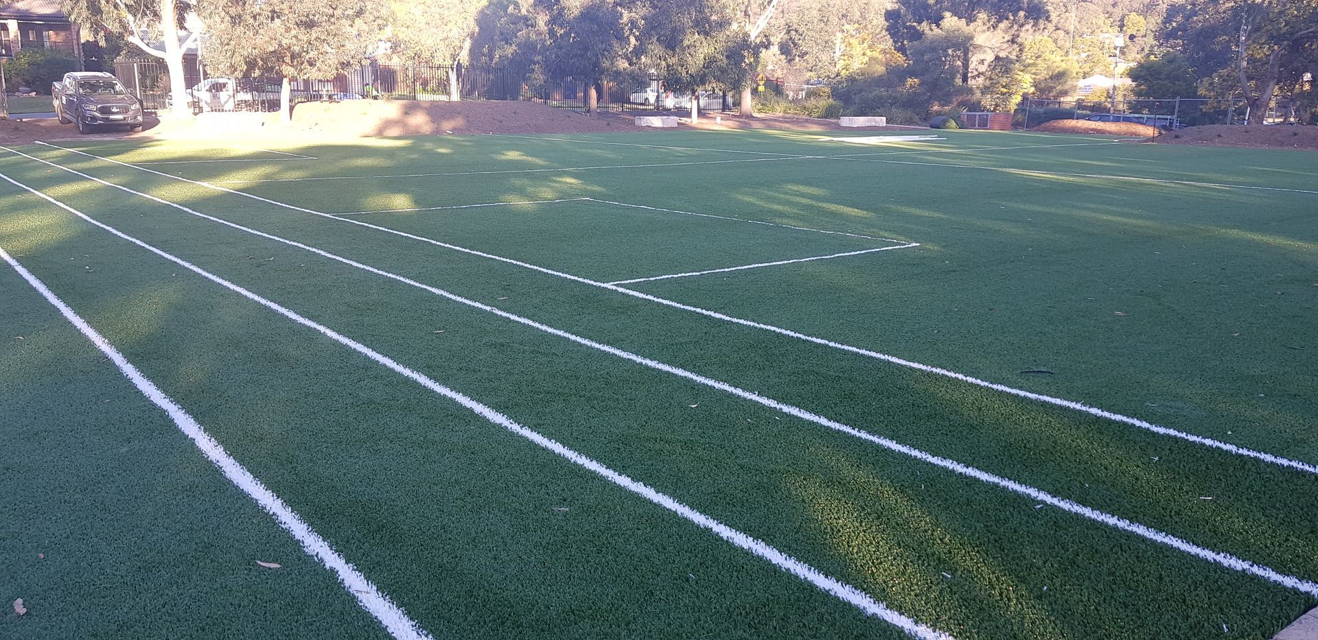 Empty green sports field with white lane markings and trees in the background