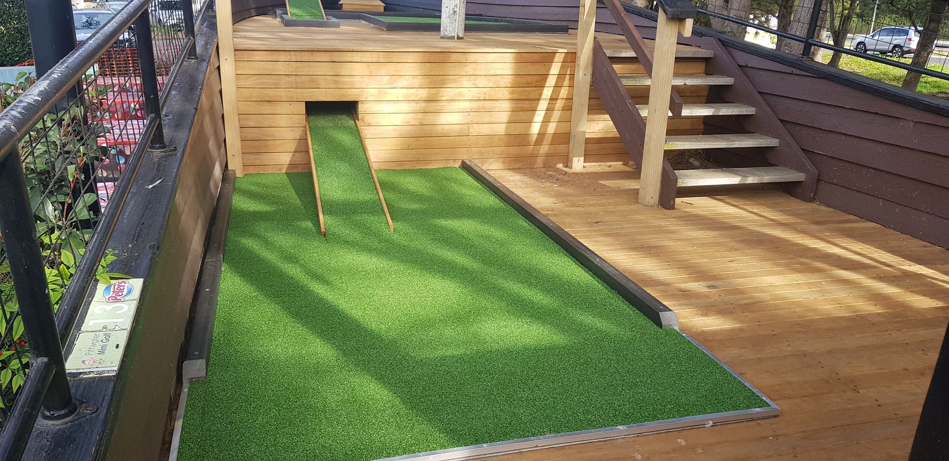 Outdoor deck with artificial grass, wooden stairs, and railings in sunlight