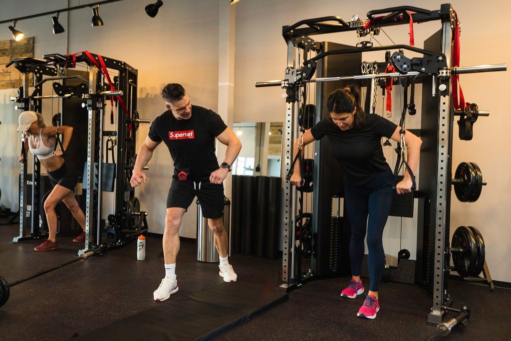 Superset Fitness owner and trainer Greg Stotz teaching a client how to use the cable machine for a chest press.