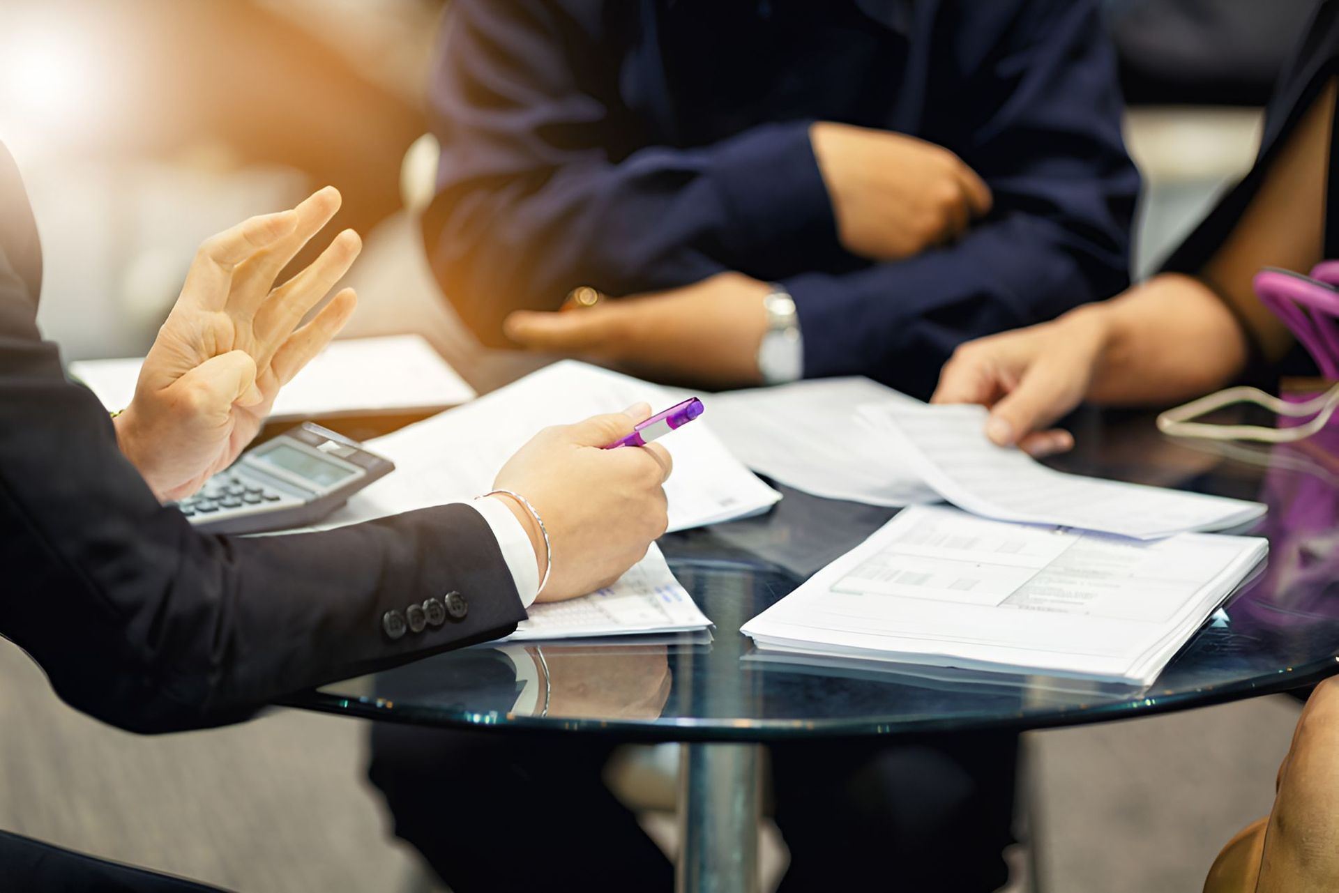 A Group Of People Are Sitting Around A Table With Papers And A Calculator — Grant Finance Solutions In Toowoomba, QLD