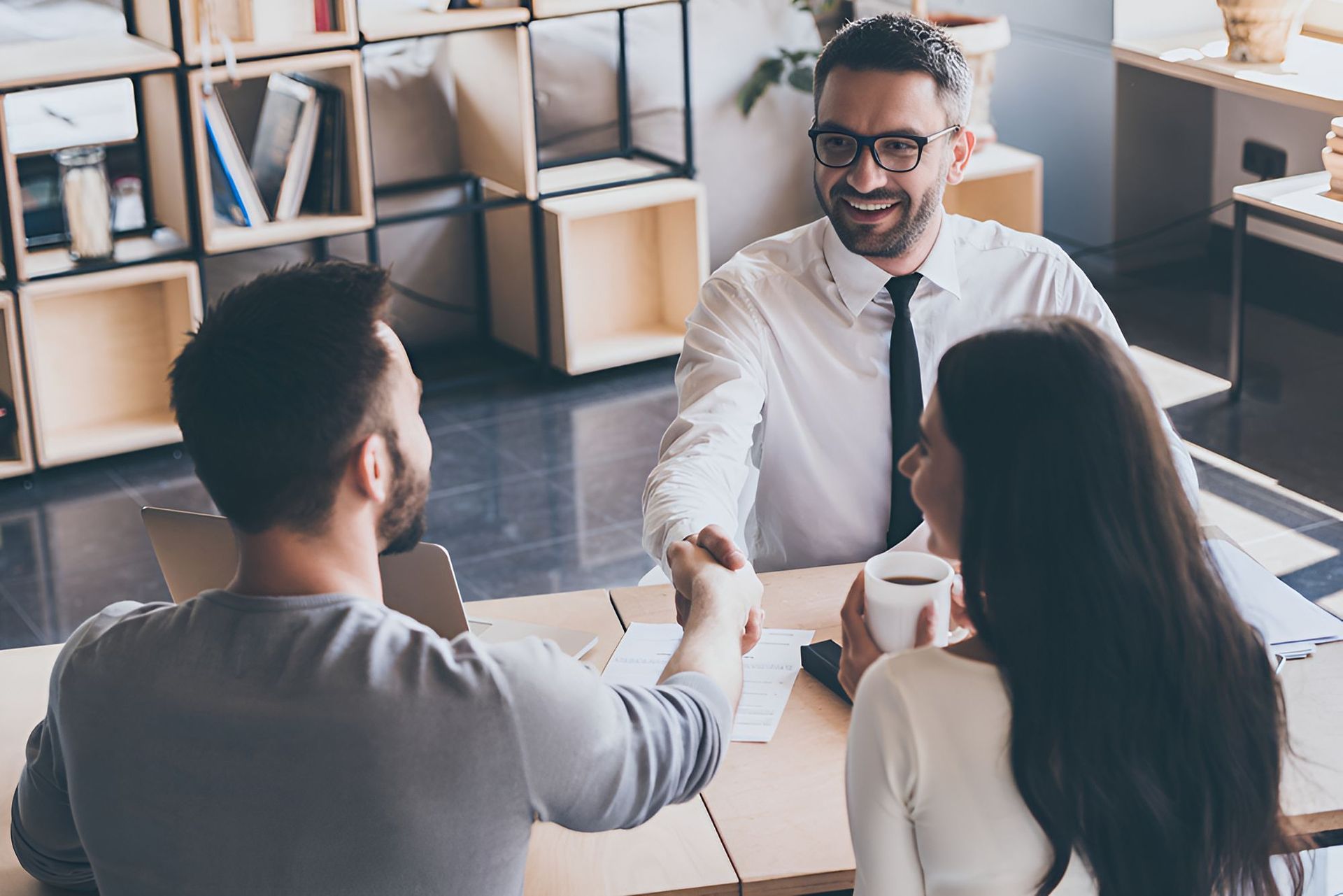 A Man Is Shaking Hands With A Woman While Sitting At A Table — Grant Finance Solutions In Toowoomba, QLD