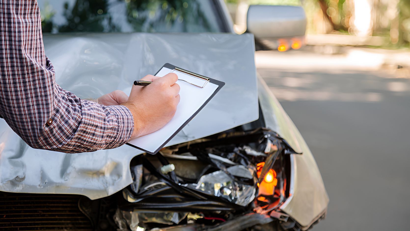 A Man Is Writing On A Clipboard In Front Of A Damaged Car — Grant Finance Solutions In Gold Coast, QLD