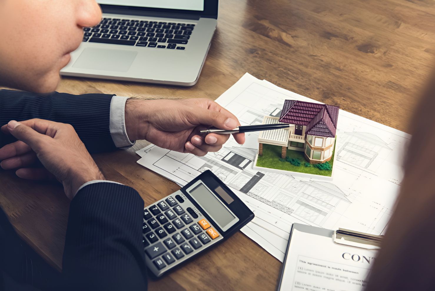 A Man Is Sitting At A Table With A Calculator And A Model House — Grant Finance Solutions In Highlands, QLD
